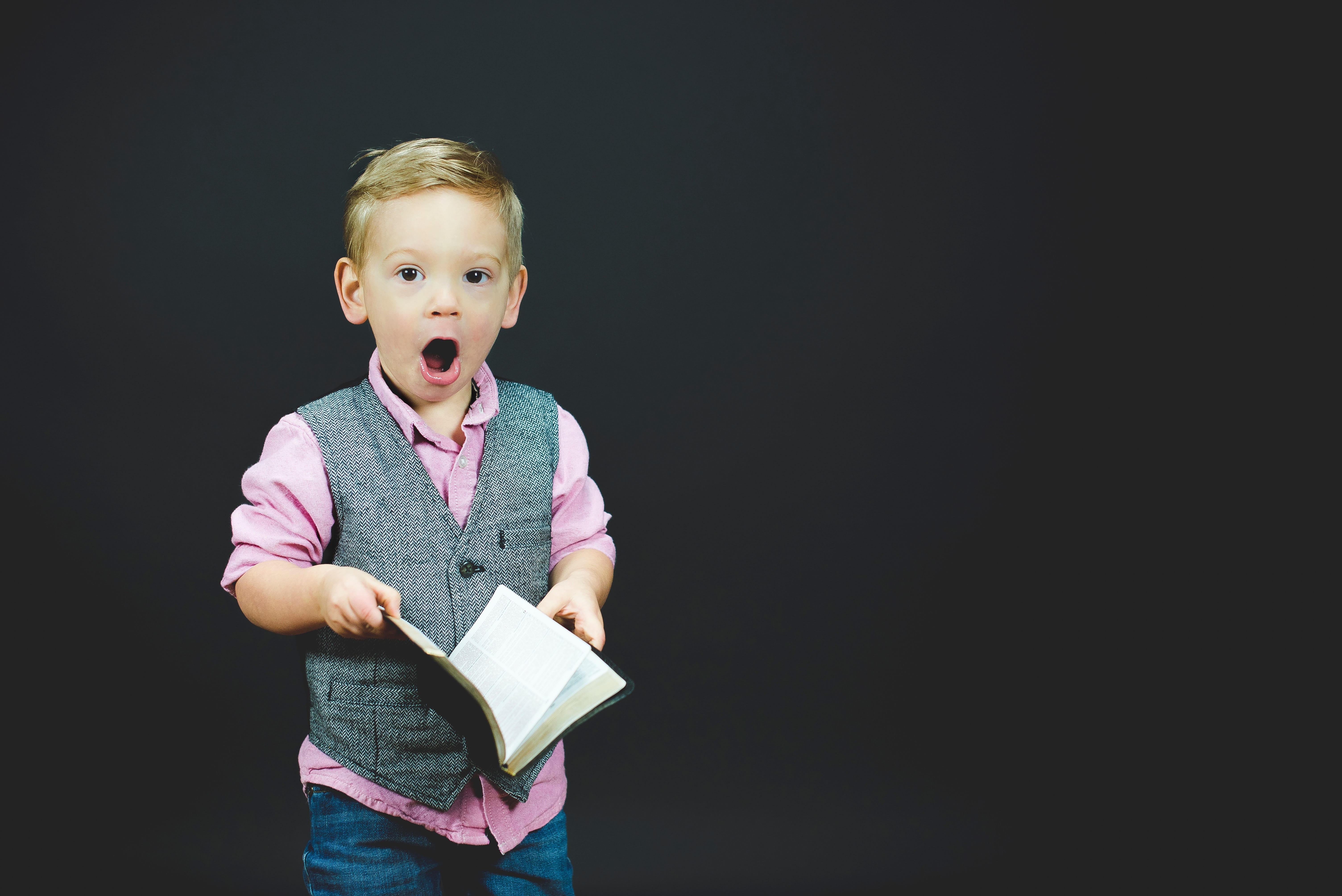 a surprised little boy in a vest holding a book