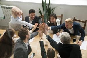 a team of professionals at a conference table leaning in for a group high five