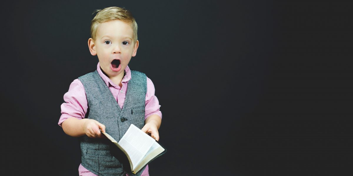 a surprised little boy in a vest holding a book