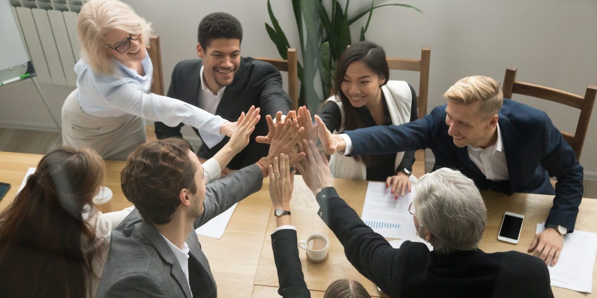 a team of professionals at a conference table leaning in for a group high five