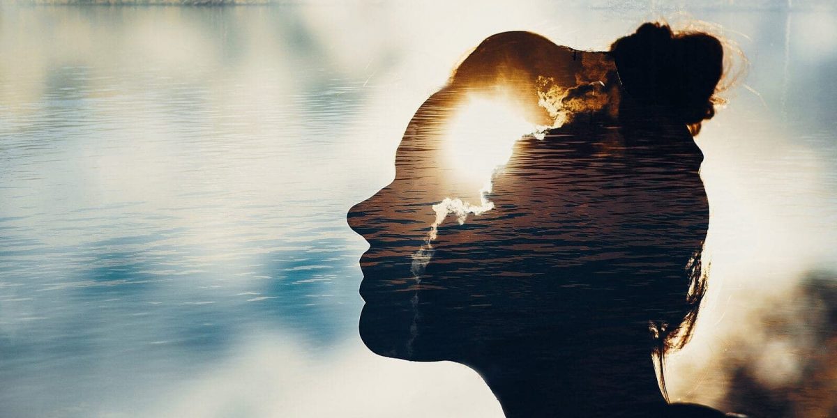 a silhouette of a woman overlaid with a lake and the sun partially hidden by clouds