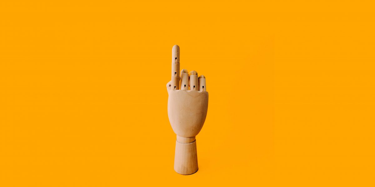 a puppet hand with the index finger pointing up on an orange background