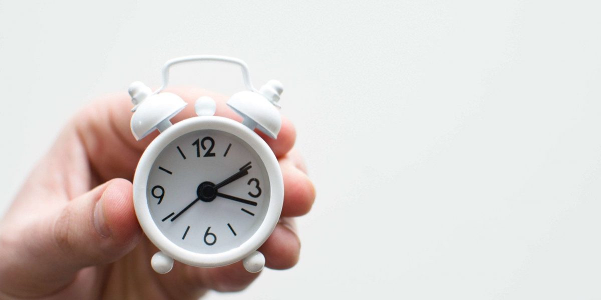 A hand holding a small white alarm clock