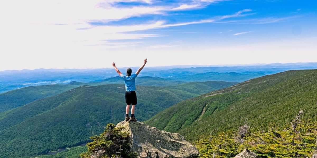 man celebrating with his hands in the air standing on top of a mountain